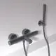 Schwarzes Badethermostat mit zwei runden Griffen und einem Handbrauseanschluss, montiert an einer hellen Wand. Produkt von Ideal Standard.